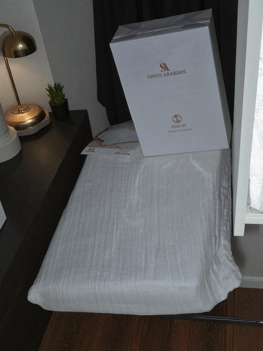 Coffret parfum Swiss Arabian posé sur un drap en coton blanc, ambiance minimaliste et élégante