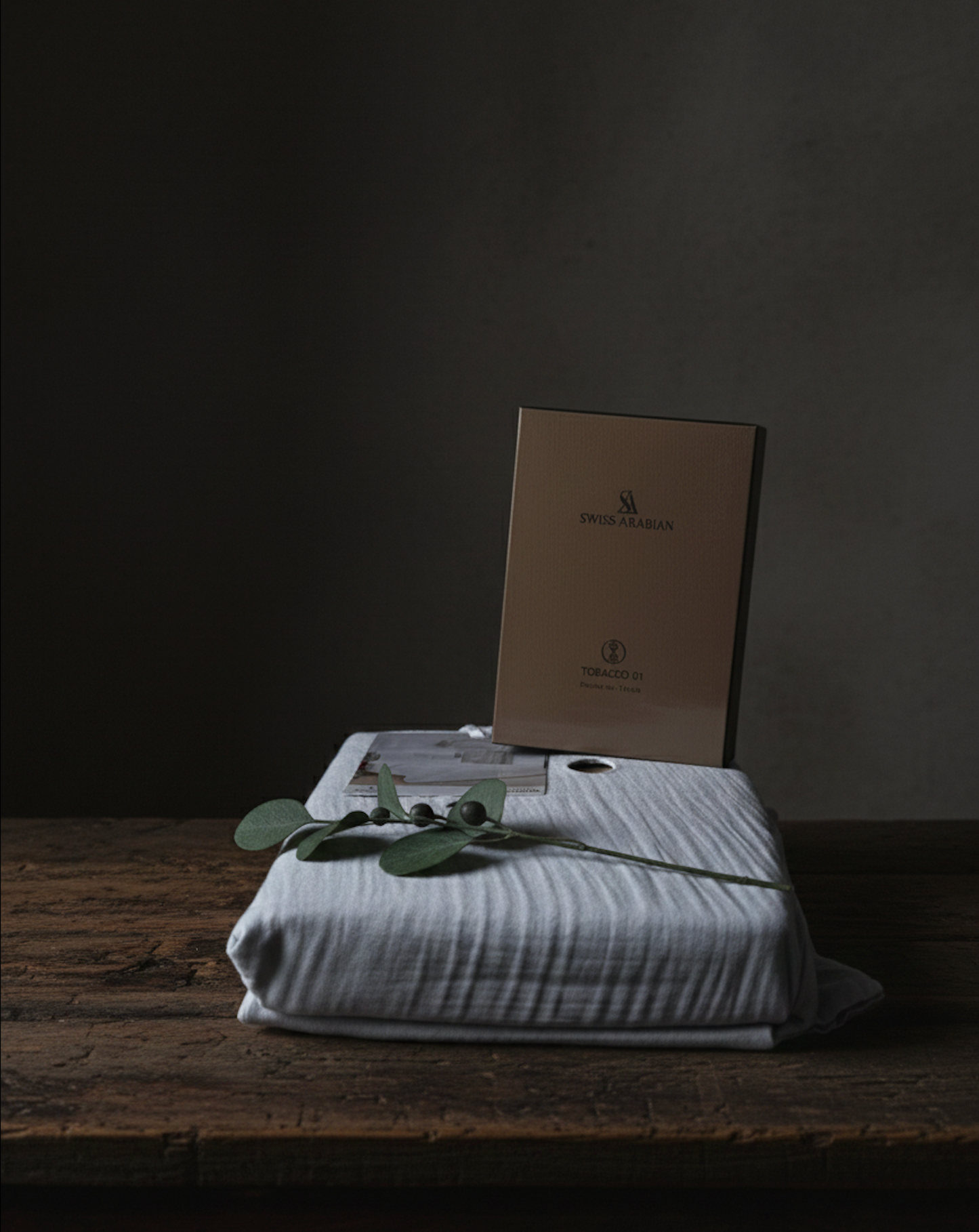 Coffret parfum Swiss Arabian sur drap en coton clair posé sur une table en bois, décoration naturelle